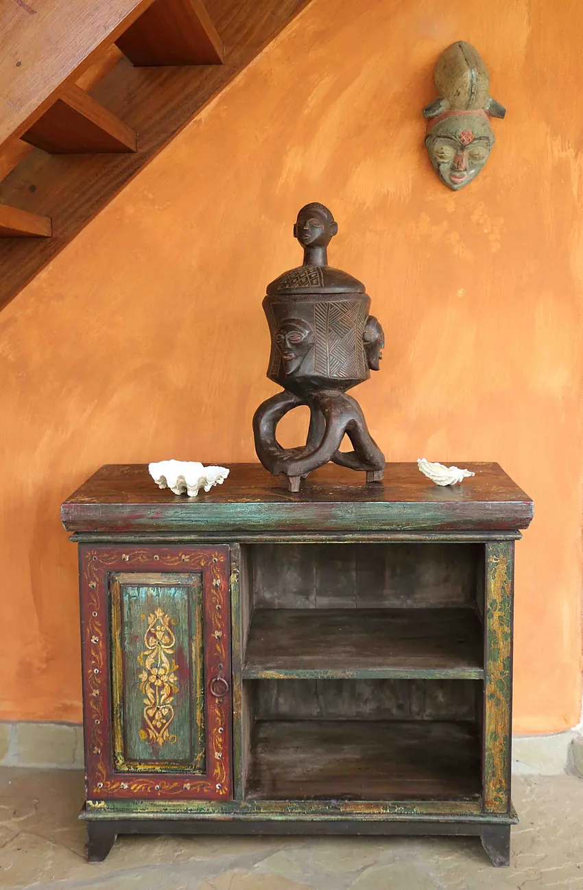 Carved standing figure on a painted cabinet against an orange wall