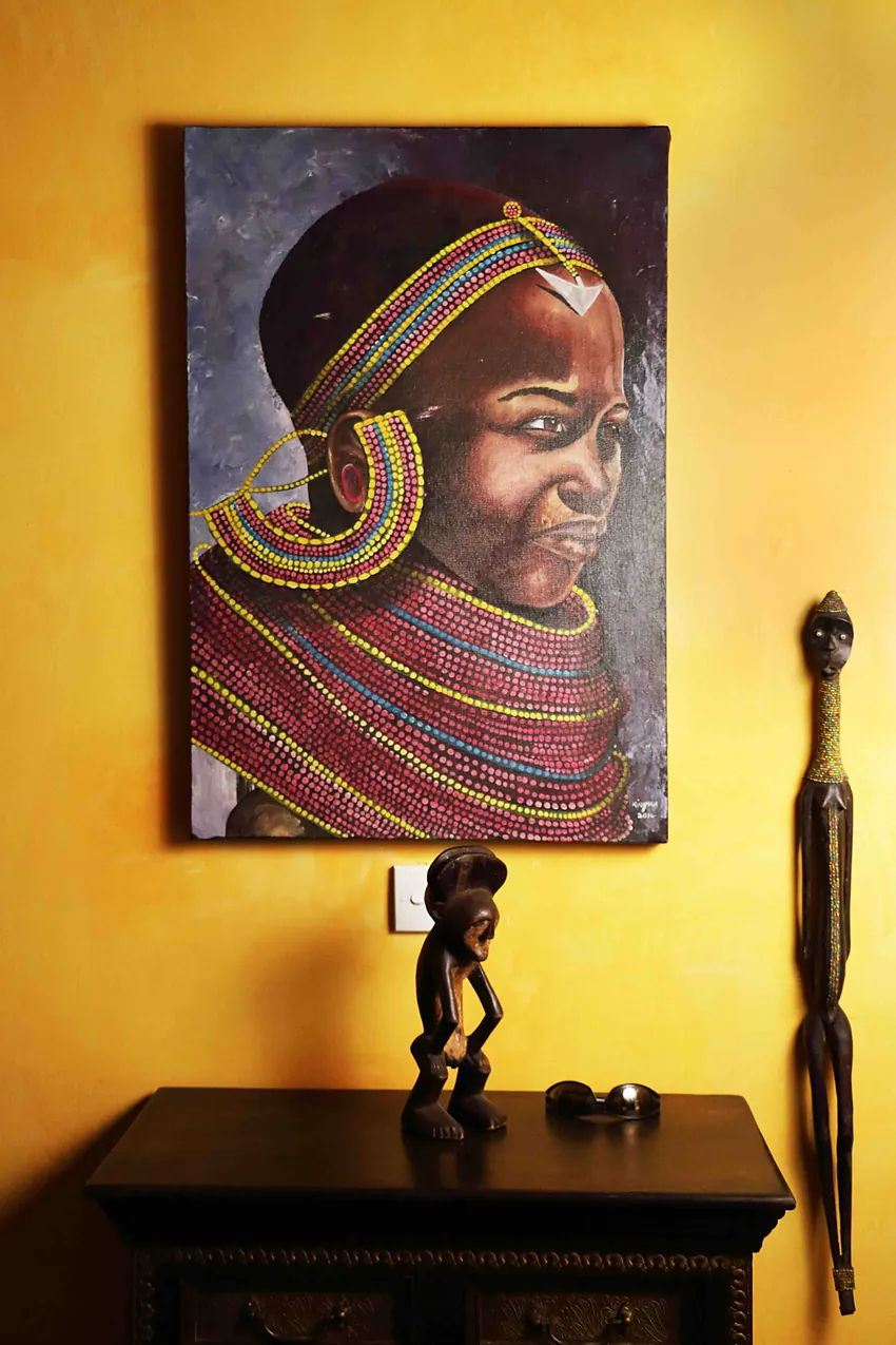 Beaded Maasai portrait painting on a yellow wall above a dark console