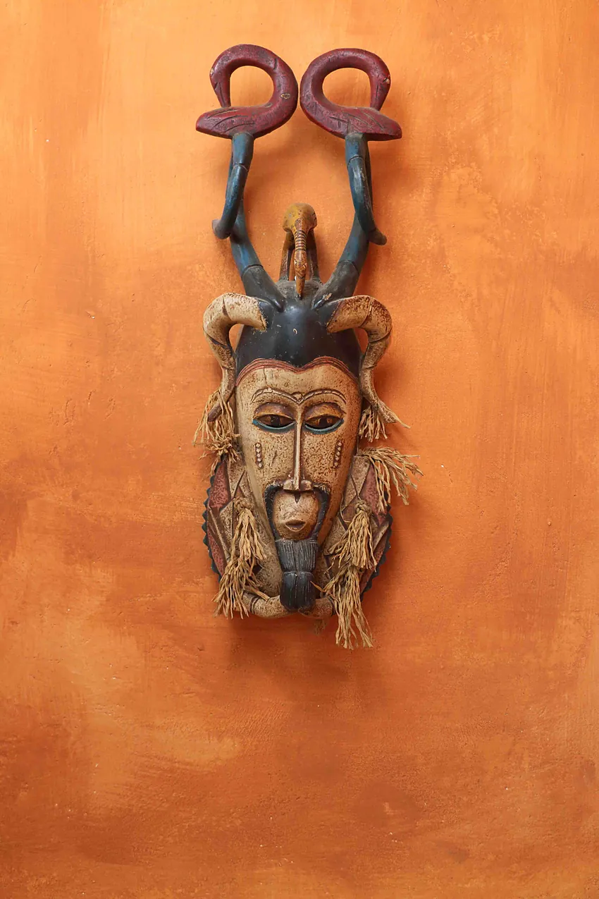 Carved mask mounted on an orange wall