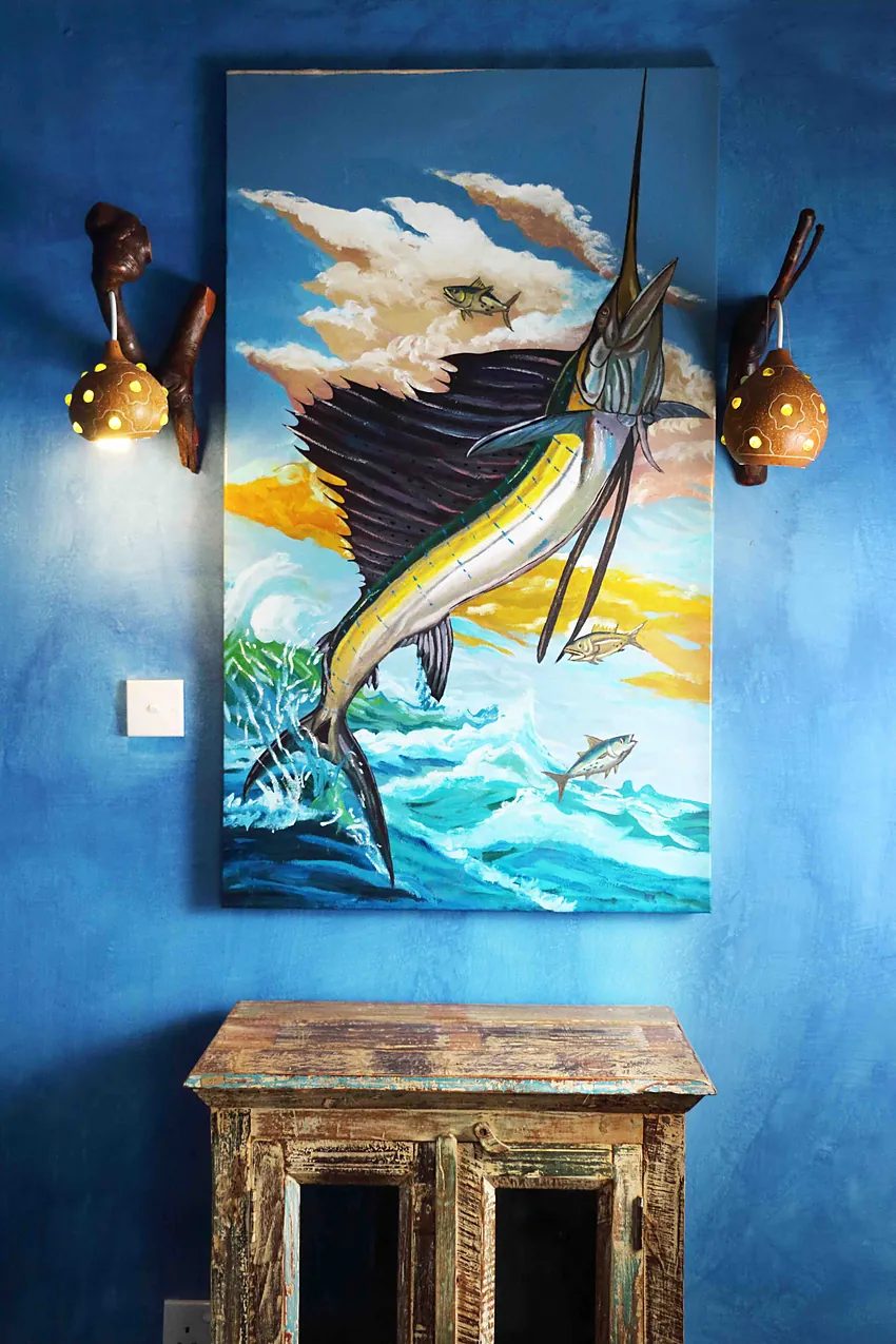 Framed sailfish painting on a blue wall above a carved console