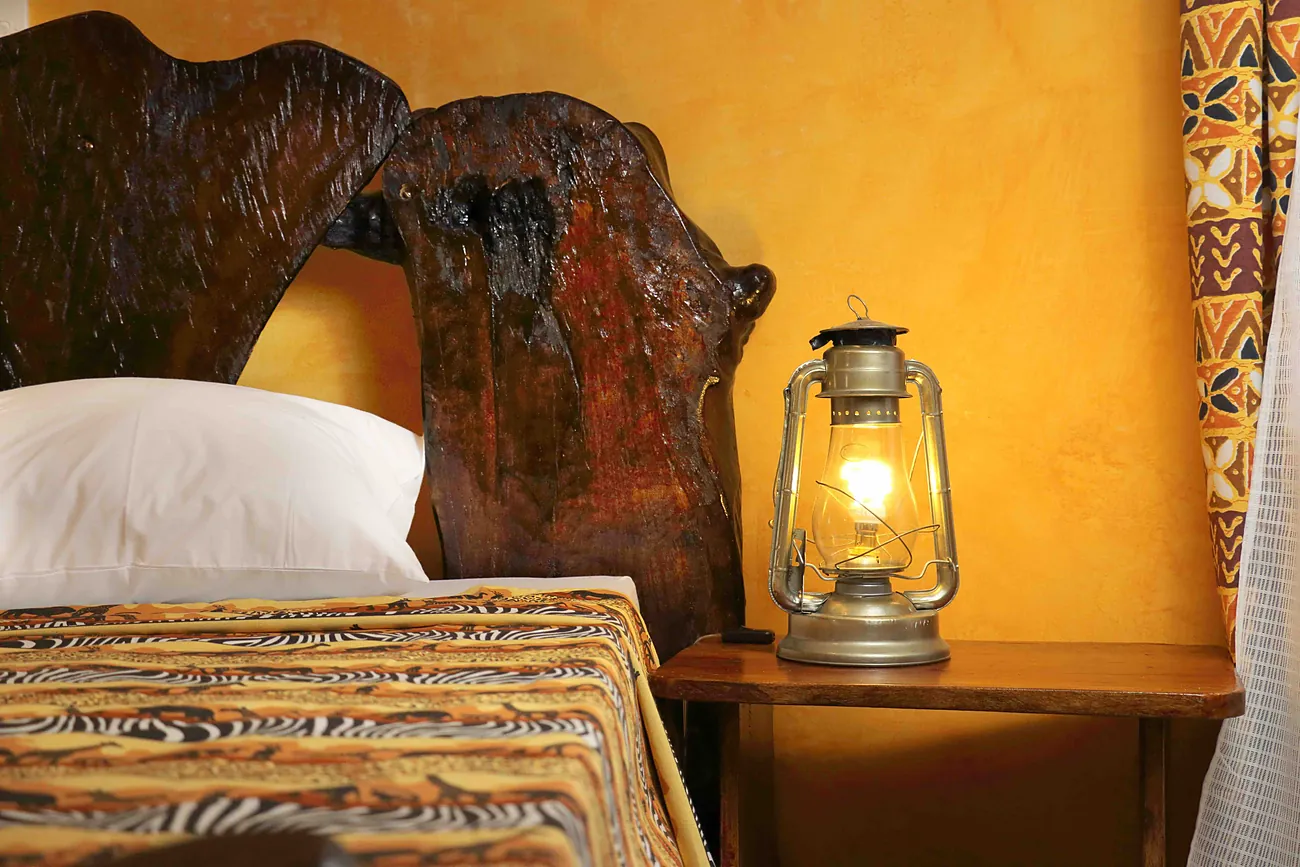 Carved dark-wood headboard against a yellow wall, hurricane lantern beside the bed